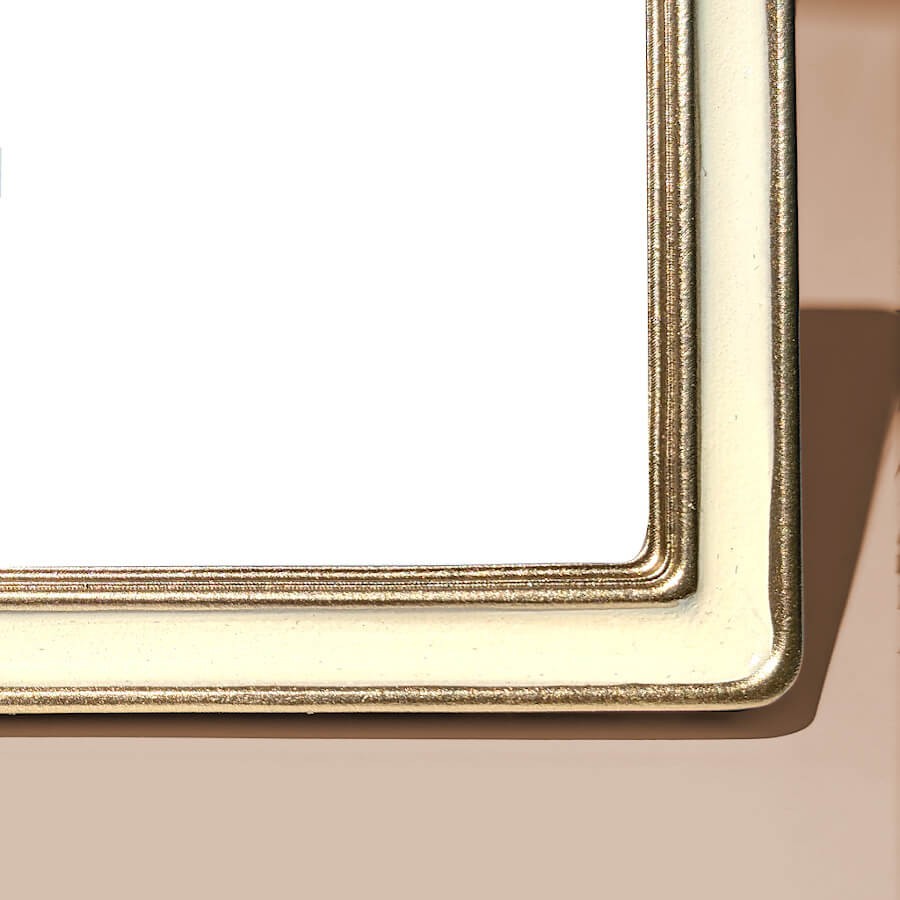 Zoom moulure d'angle : Gros plan sur la finition émaillée lisse crème et la double dorure fine du cadre.