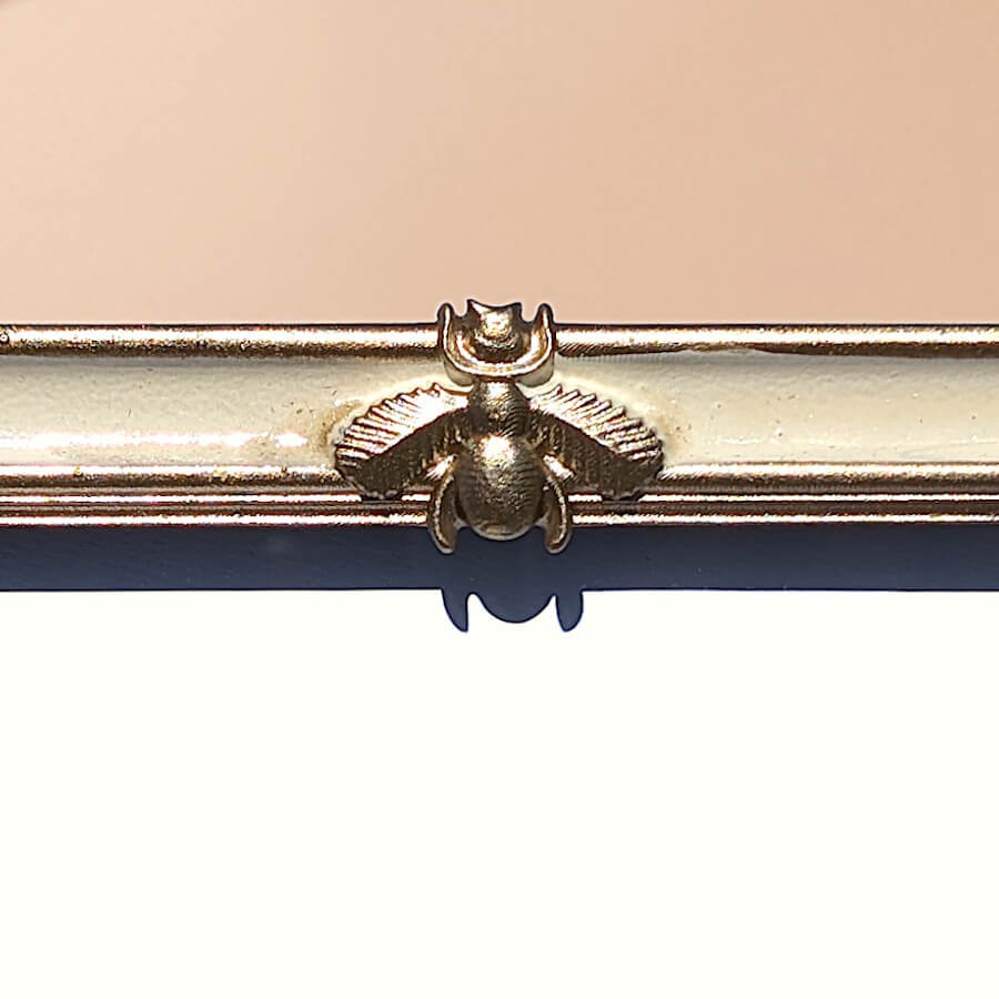 Macro relief abeille : Zoom détaillé sur la sculpture de l'abeille dorée, symbole de style Empire, fixée au sommet du cadre.