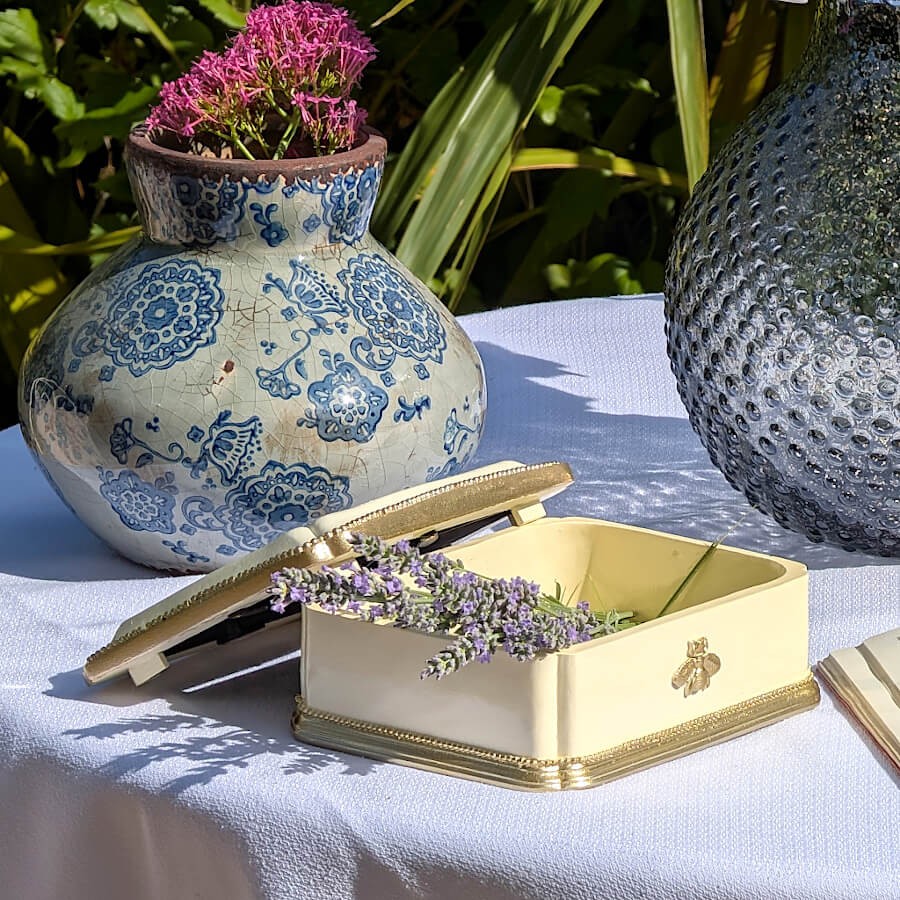 Décoration extérieure estivale : Écrin en céramique crème avec brins de lavande sur table de jardin avec nappe blanche.