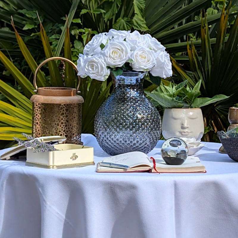 Mise en scène printanière : Coffret à bijoux abeille près d'un grand vase en verre bleu et de roses blanches.