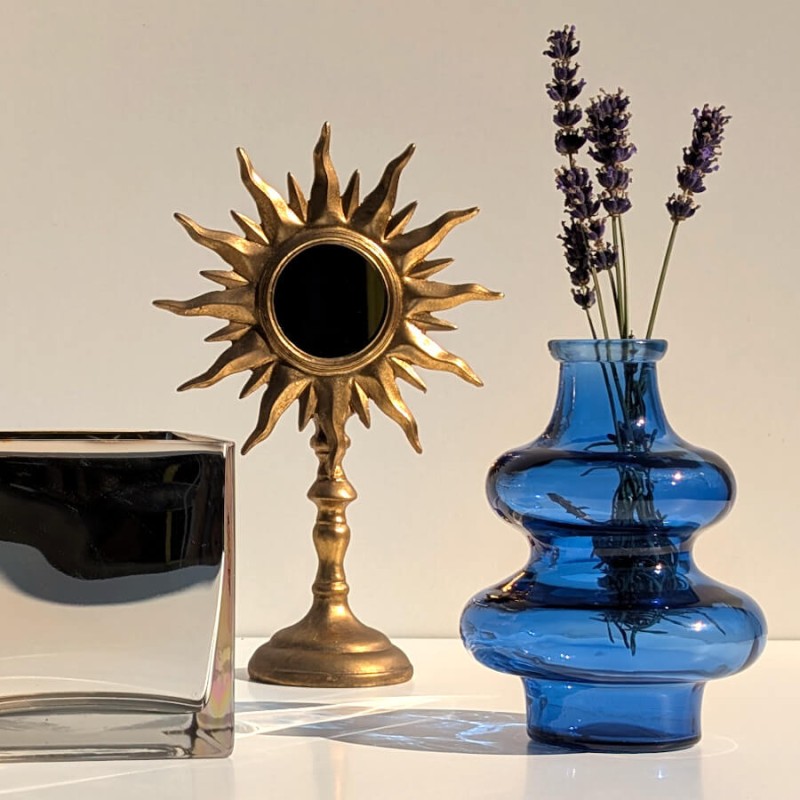 Mise en scène mystique : Miroir soleil sur pied doré près d'un vase bleu en verre et de brins de lavande.