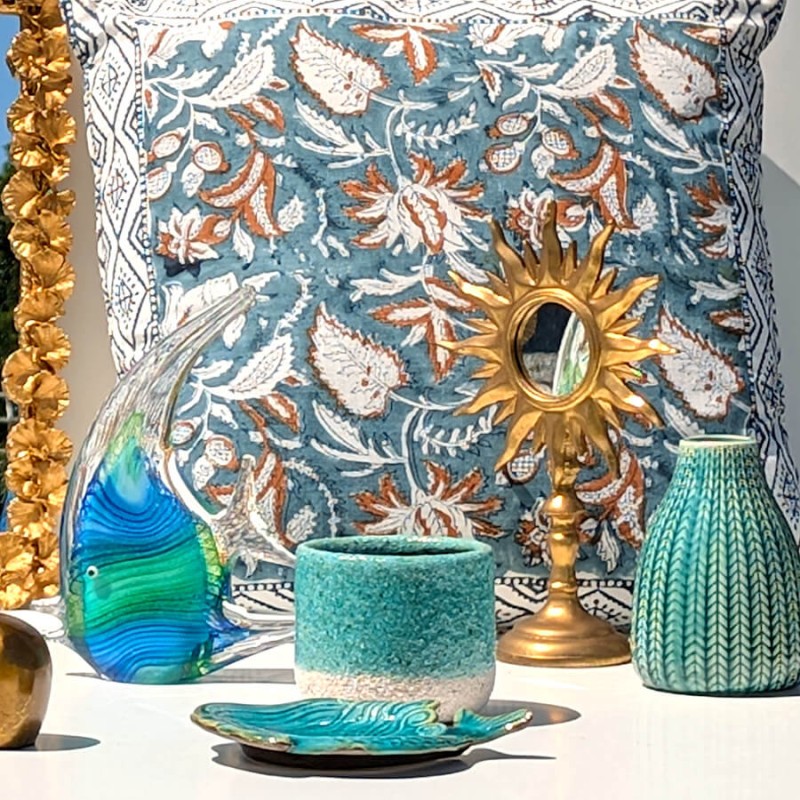 Harmonie ethnique chic : Miroir de table soleil associé à un grand coussin à motifs bleus et un vase turquoise.