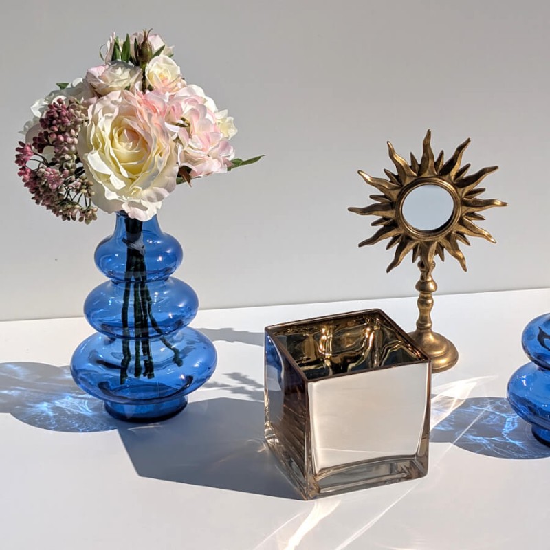 Miroir soleil doré mis en scène avec un photophore cube à effet miroir et un vase bleu, collection Deco-Delight.