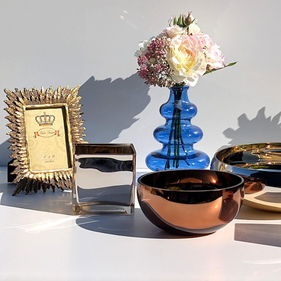 Scénographie sur table avec le modèle doré, un cadre baroque, un bol cuivré et un vase bleu.