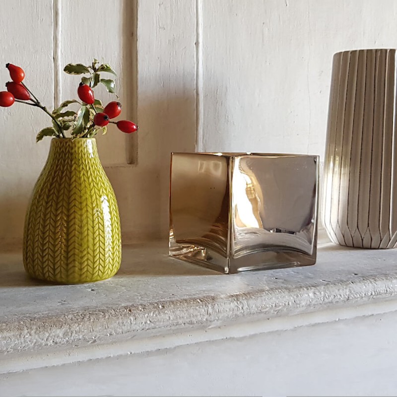 Le photophore cube doré posé sur une cheminée à côté d'un petit vase jaune épi Deco Delight.