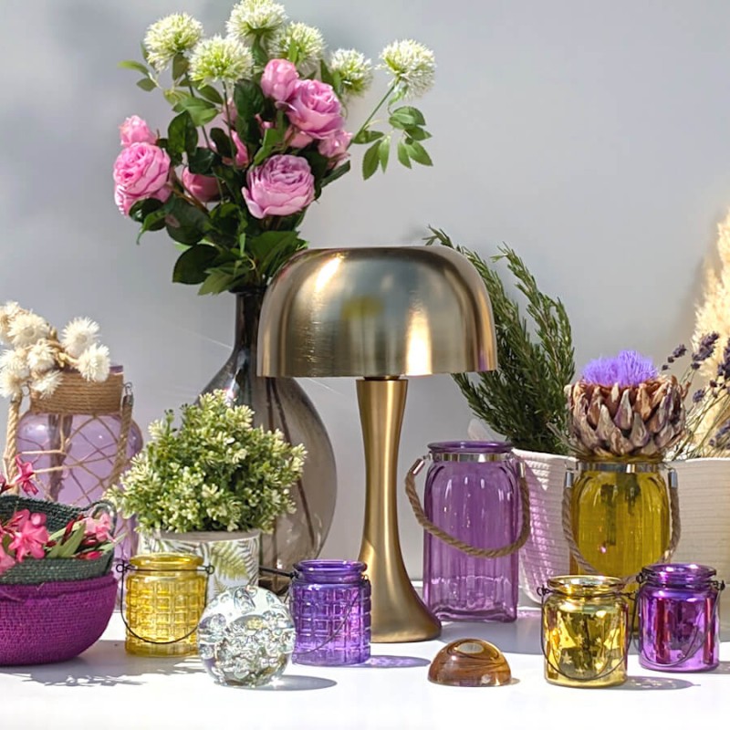 Mise en scène lumineuse : Photophores en verre violet et jaune encadrant une lampe champignon dorée.