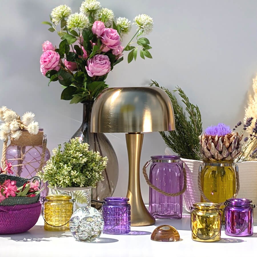 Mise en scène lumineuse : Photophores en verre violet et jaune encadrant une lampe champignon dorée.