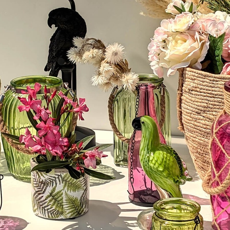 Scène tropicale : Lanterne verte à côté d'un vase motif feuilles et d'un perroquet décoratif vert.
