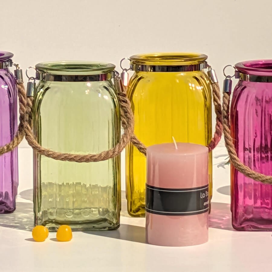 Alignement de couleurs : Lanternes en verre vert, jaune et rose entourant une grosse bougie pilier rose.