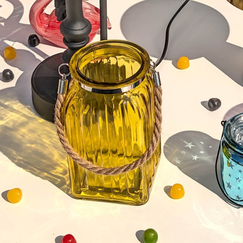 Scène lumineuse rasante : Lanterne en verre jaune capturant les rayons du soleil et projetant des ombres géométriques.