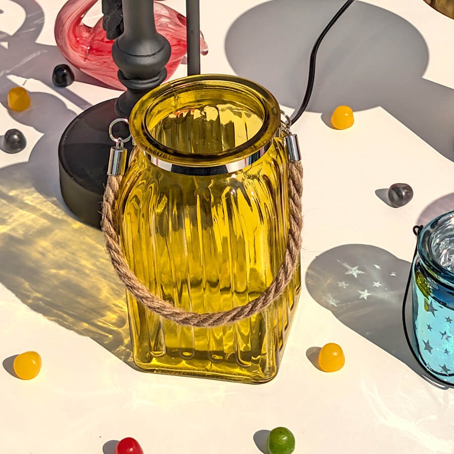 Scène lumineuse rasante : Lanterne en verre jaune capturant les rayons du soleil et projetant des ombres géométriques.