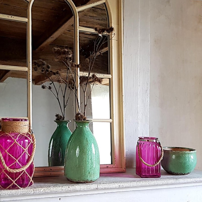Scénographie cheminée : Composition élégante mariant deux vases en verre vert d'eau et des photophores fuchsia.