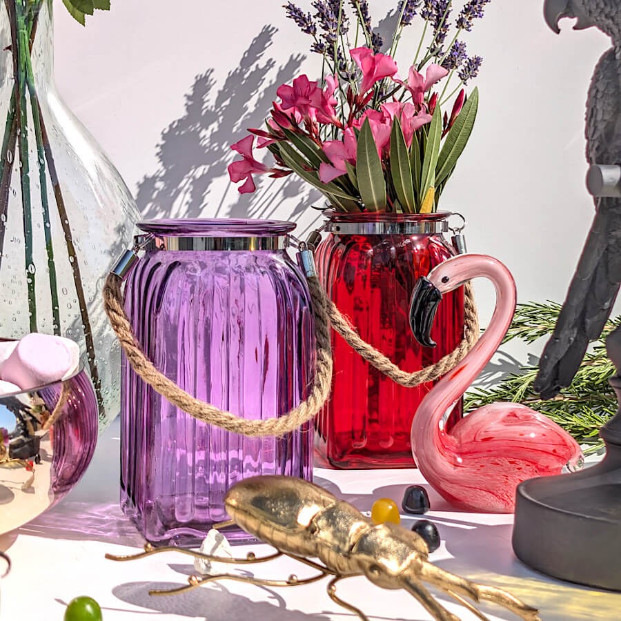 Scène estivale mariant un vase violet, un photophore rouge garni de fleurs et une statuette flamant rose.