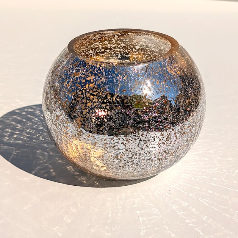 Photophore boule en verre craquelé posé en extérieur sous une lumière vive du soleil.