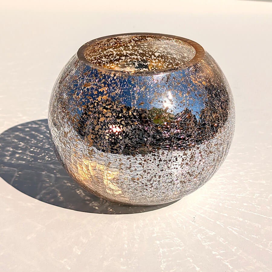 Photophore boule en verre craquelé posé en extérieur sous une lumière vive du soleil.