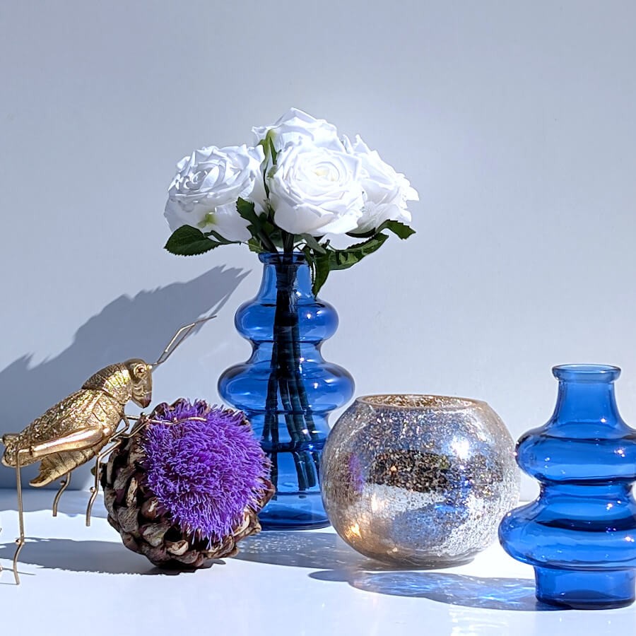 Scénographie avec une statuette sauterelle dorée, le photophore craquelé et deux vases en verre bleu Deco-Delight.