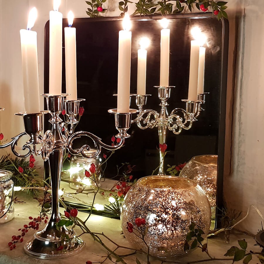 Ambiance festive avec un candélabre argenté à 5 branches, des bougies blanches allumées et le photophore craquelé.