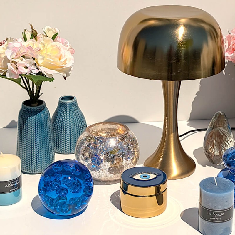 Composition sur table blanche avec vases bleus, roses blanches, le photophore craquelé, une bougie et une boîte dorée.