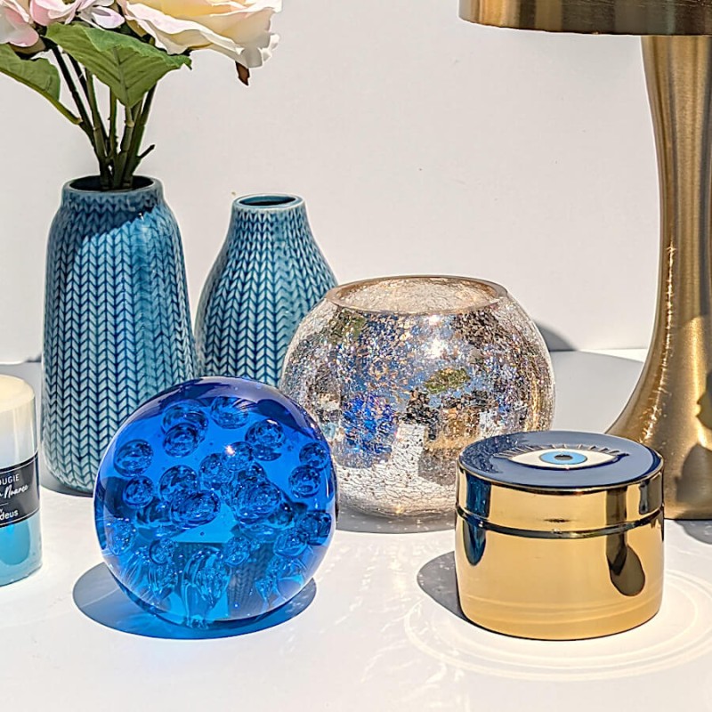 Composition estivale avec le vase bleu, le photophore craquelé, une grosse boule de verre bleu azur et la boîte dorée.