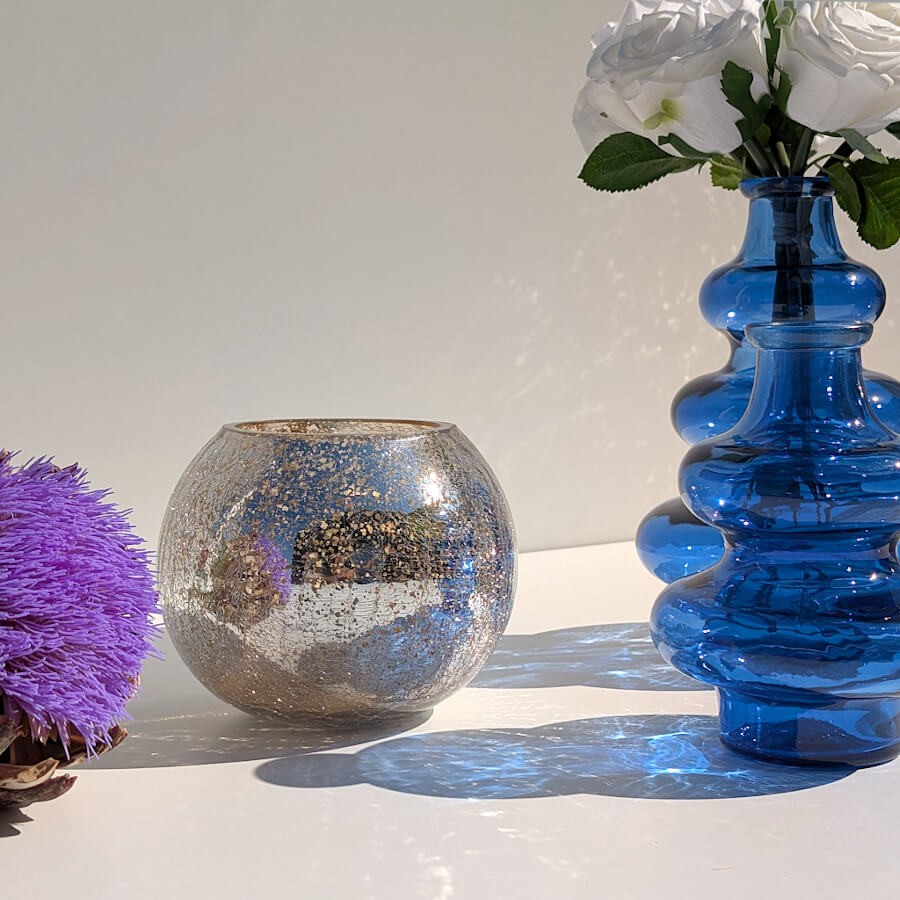 Le photophore craquelé posé à côté d'un grand vase en verre bleu à vagues Deco-Delight sur une surface blanche ensoleillée.
