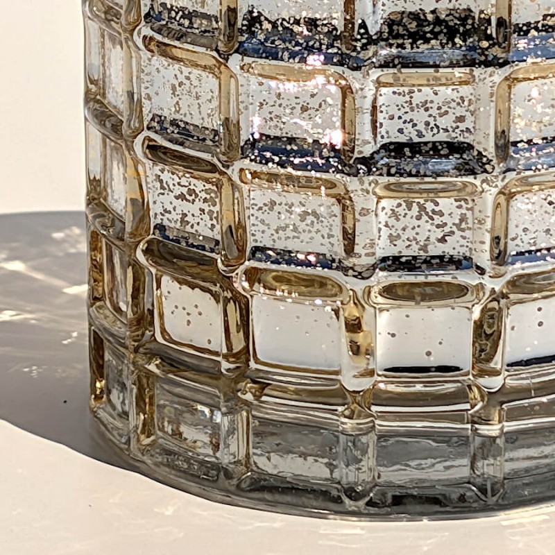 Reflets de la lumière du jour sur la structure en damier du photophore cylindrique en verre mercurisé.