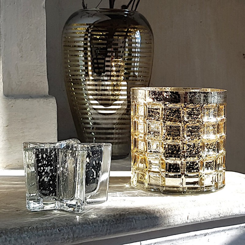 Alignement de photophores Deco Delight sur un manteau de cheminée avec un grand vase ligné Deco-Delight en arrière-plan.