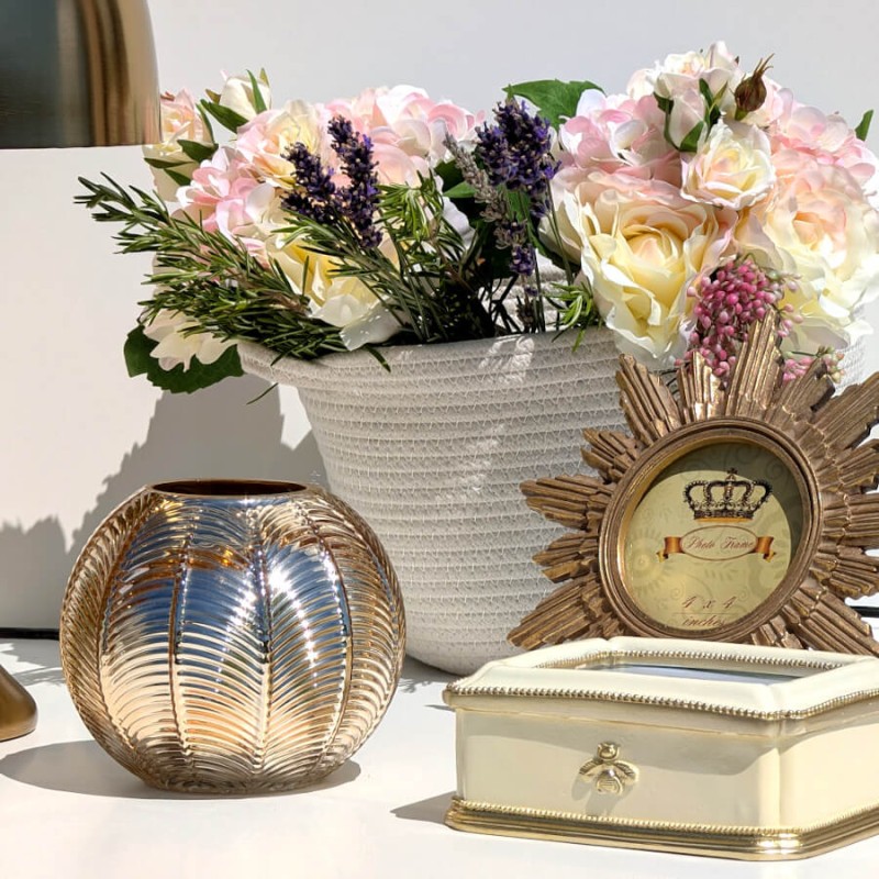 Mise en scène lumineuse : Panier tressé blanc cassé entouré d'un photophore boule doré et d'une boîte à bijoux crème.