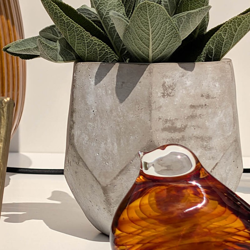 Gros plan sur le pot facetté garni d'une succulente et la sculpture d'oiseau ambré sous le soleil.