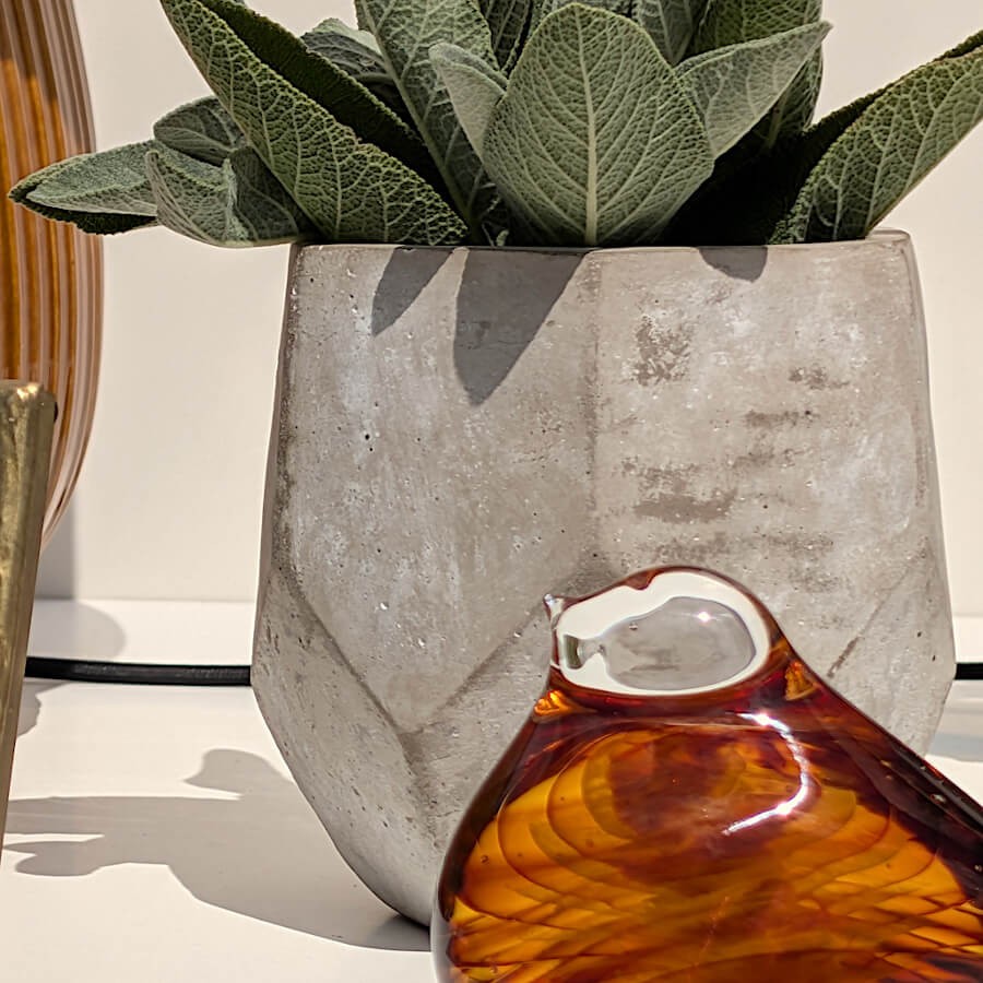 Gros plan sur le pot facetté garni d'une succulente et la sculpture d'oiseau ambré sous le soleil.