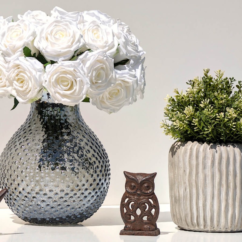 Composition de bouquets avec un vase moucheté gris rempli de roses et le pot en ciment surmonté de verdure.