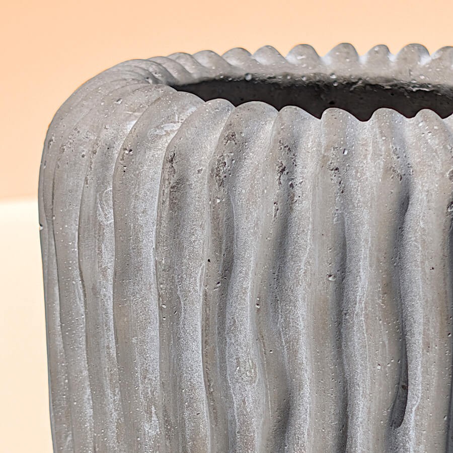 Zoom sur le col arrondi et la texture brute striée du ciment gris moulé.