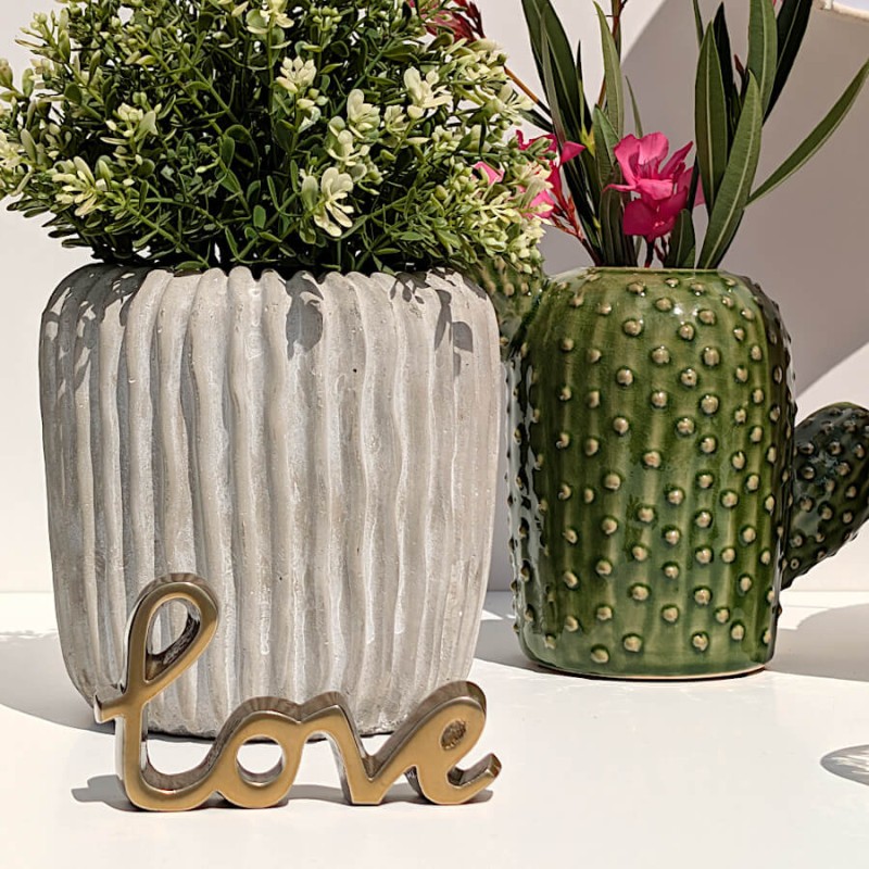 Présentation du pot en ciment à côté de la figurine Love dorée et d'un cache-pot en forme de cactus vert.