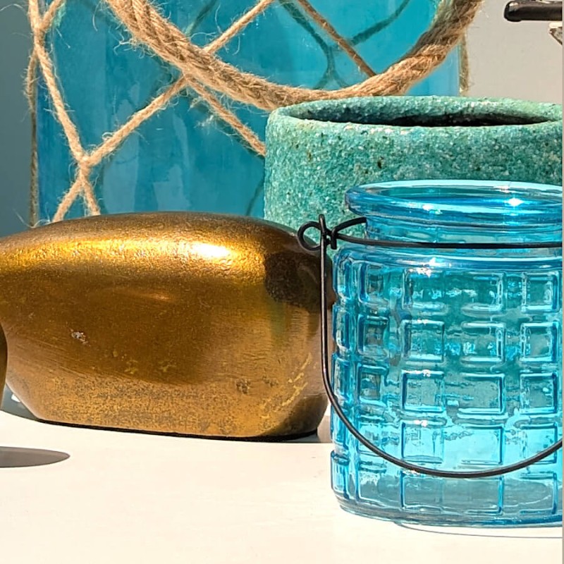 Photophore turquoise posé dans une décoration d'inspiration marine avec corde, céramique et baleine dorée.
