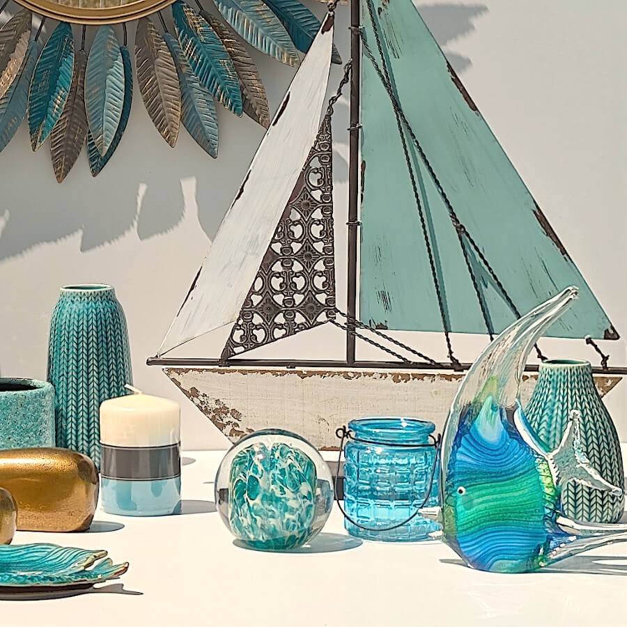 Décoration de style bord de mer avec bateau en métal, presse-papier et photophore turquoises.