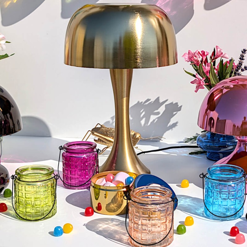 Table de fête décorée d'une lampe champignon dorée et d'un assortiment de photophores colorés.