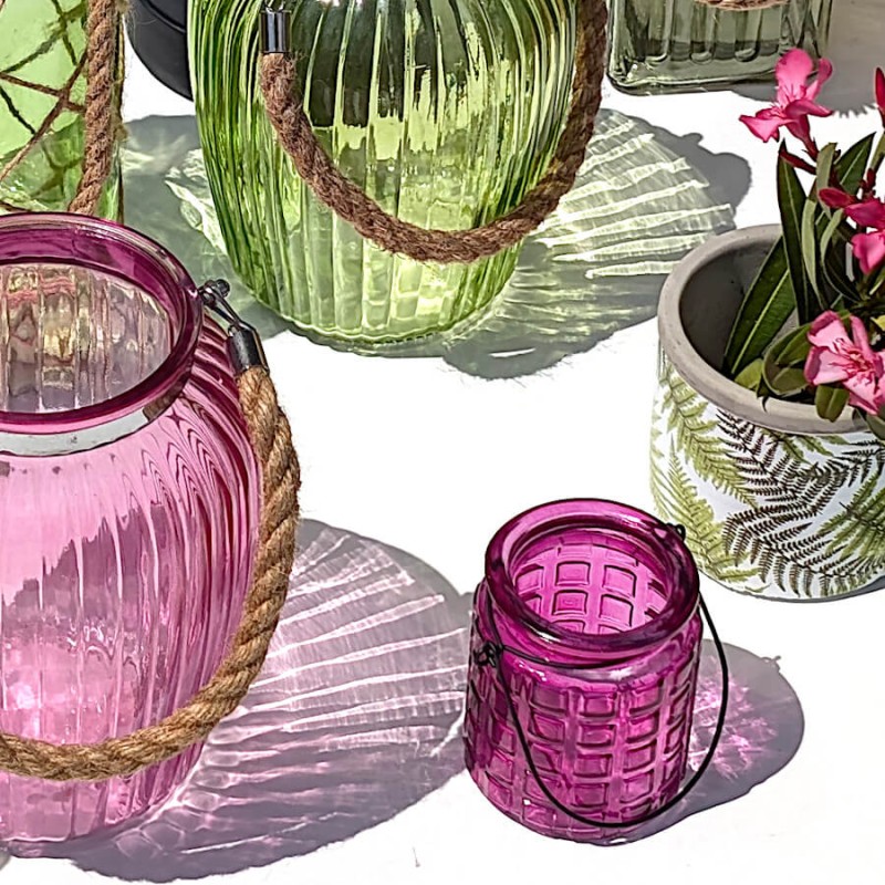 Petit photophore fuchsia en verre gaufré posé au soleil avec des vases en verre colorés.