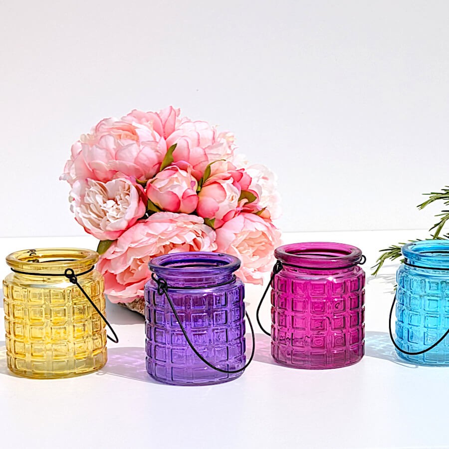 Alignement de photophores teints (jaune, violet, fuchsia, turquoise) sur fond blanc.