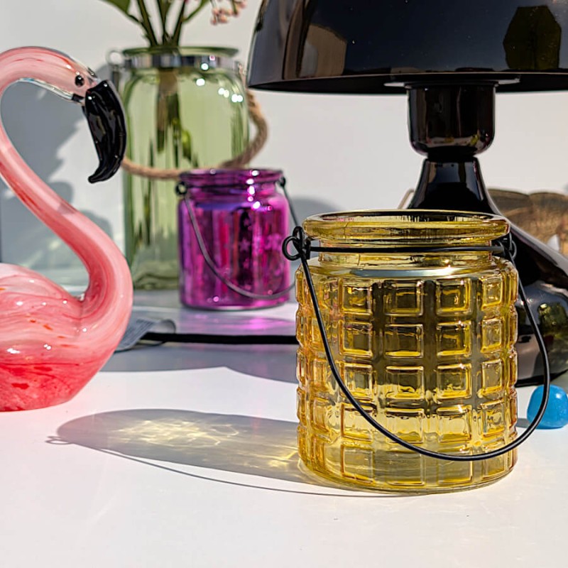 Photophore jaune baigné de lumière au côté d'une figurine flamingo en verre (également dans notre catalogue).
