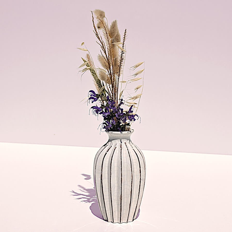 Le vase plissé blanc accueille de petites herbes séchées sur fond pastel.