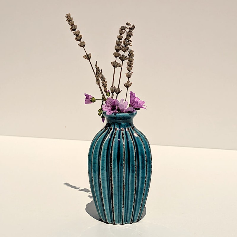 Le vase plissé turquoise accueille de petites fleurs de lavande sur fond clair.