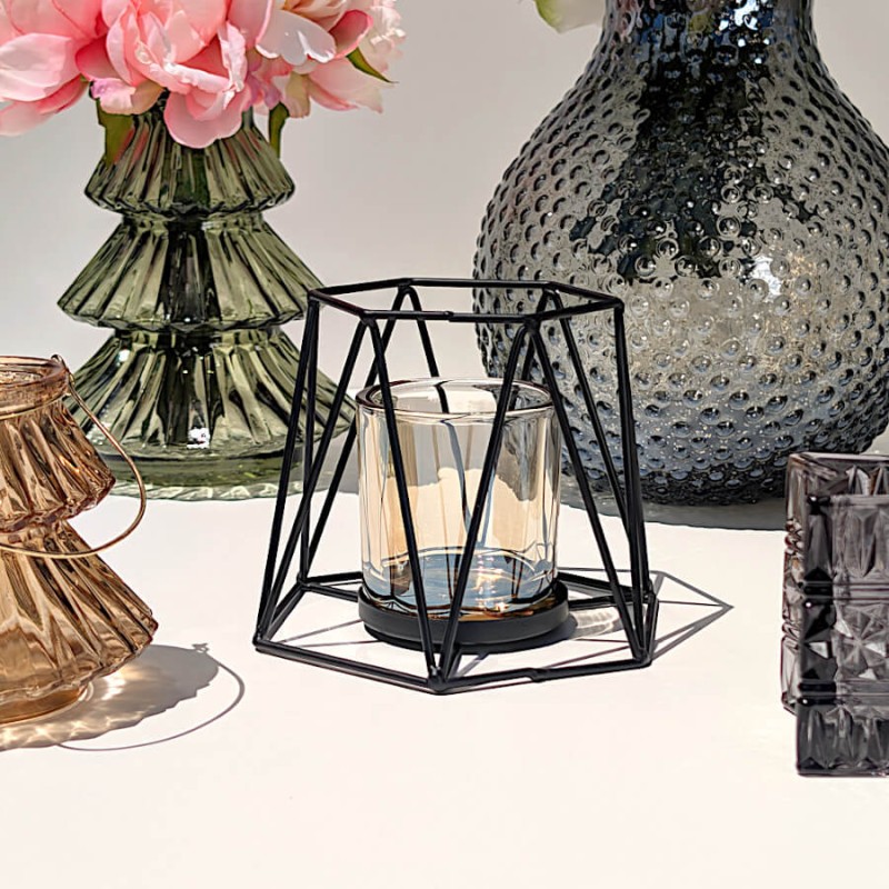 Présentation du photophore hexagonal entouré d'un vase vert floral et d'un vase en verre gris moucheté sous le soleil.
