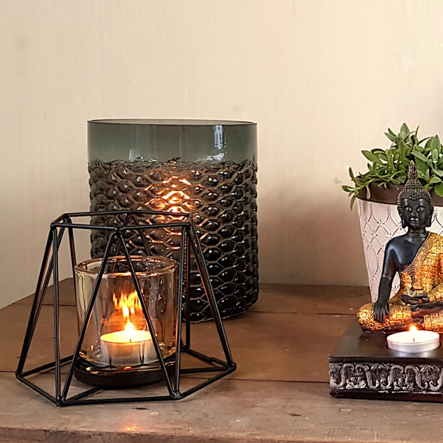 Ambiance zen et apaisante associant le photophore allumé à une statuette de Bouddha et une plante verte.