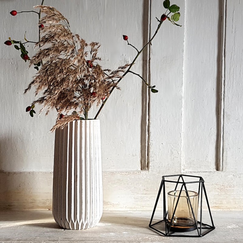 Scénographie épurée sur manteau de cheminée avec le photophore hexagonal posé à côté d'un grand vase blanc cannelé.