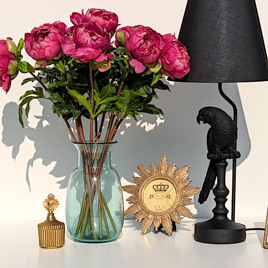 Cadre photo rond motif soleil doré posé à côté d'un vase en verre bleu et d'une boîte ex-voto.