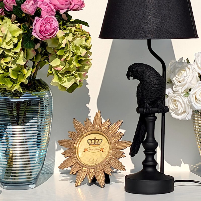 Scénographie Deco Delight chic associant le cadre soleil doré à la lampe perroquet noir et un vase garni de fleurs.