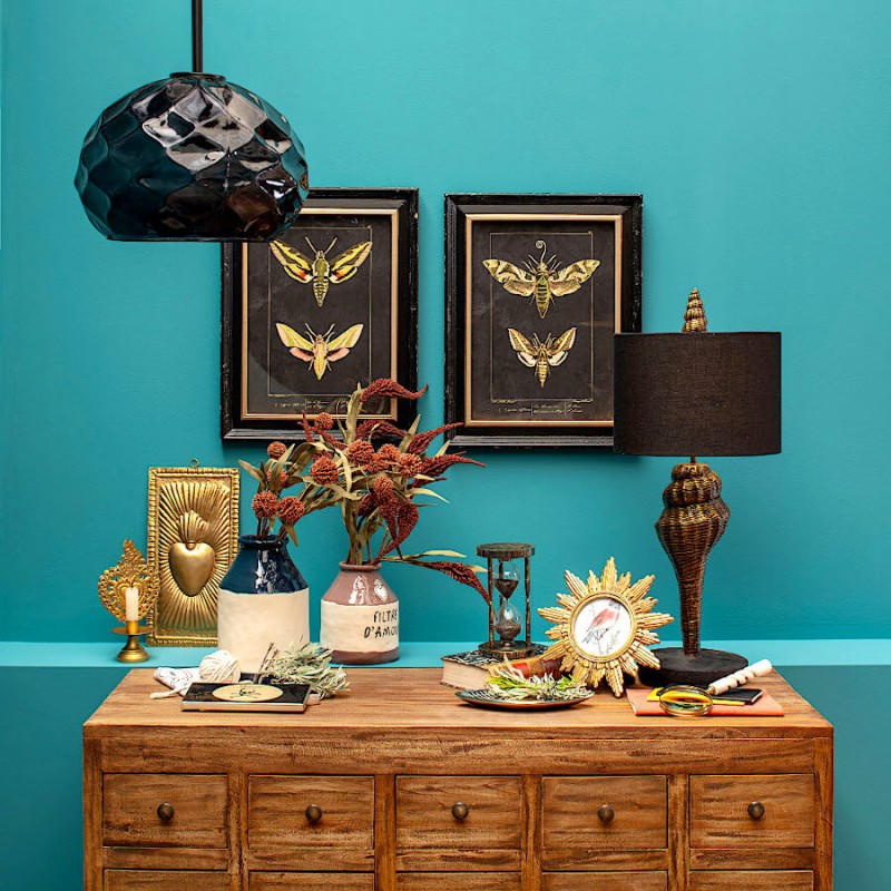 Vue d'ensemble d'un buffet décoré avec le cadre soleil doré, des cadres muraux et une lampe noire.