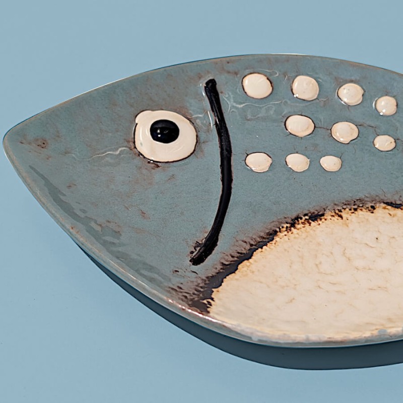 Gros plan sur les détails peints et la texture grésée du plat poisson en céramique.