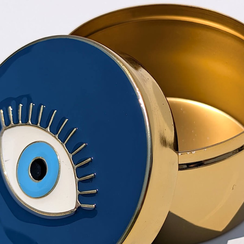 Gros plan sur le couvercle émaillé bleu nuit et cils dorés de la boîte œil protecteur du catalogue Deco-Delight.