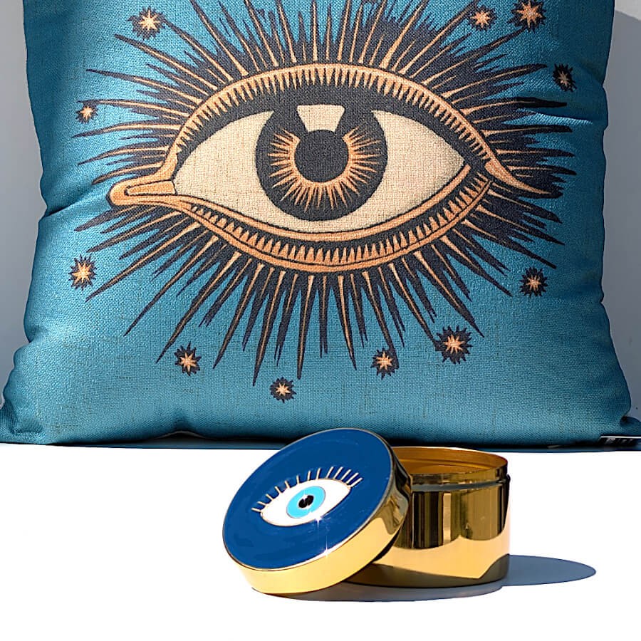 Boîte dorée œil protecteur associée à un coussin bleu brodé d'un motif œil mystique.