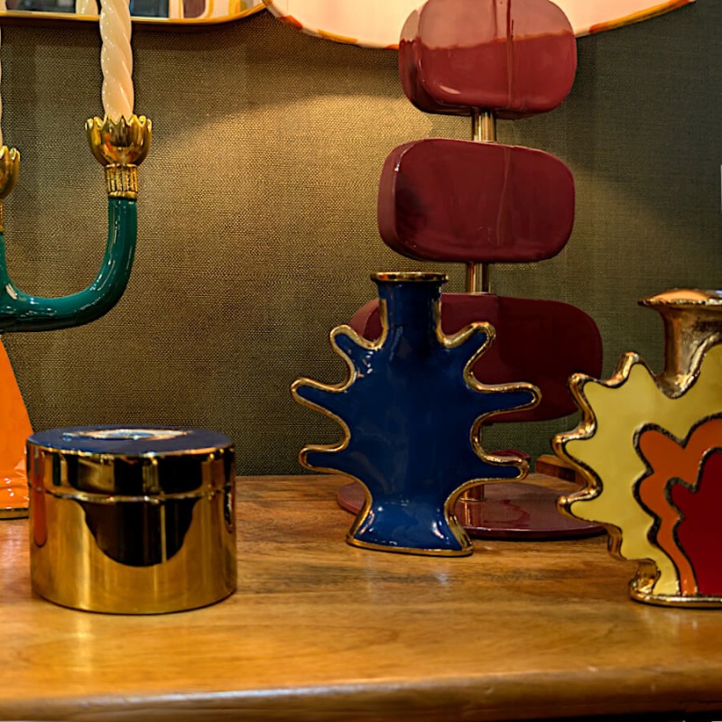 Boîte œil dorée sur buffet en bois entourée de vases en céramique graphiques et bougeoirs.